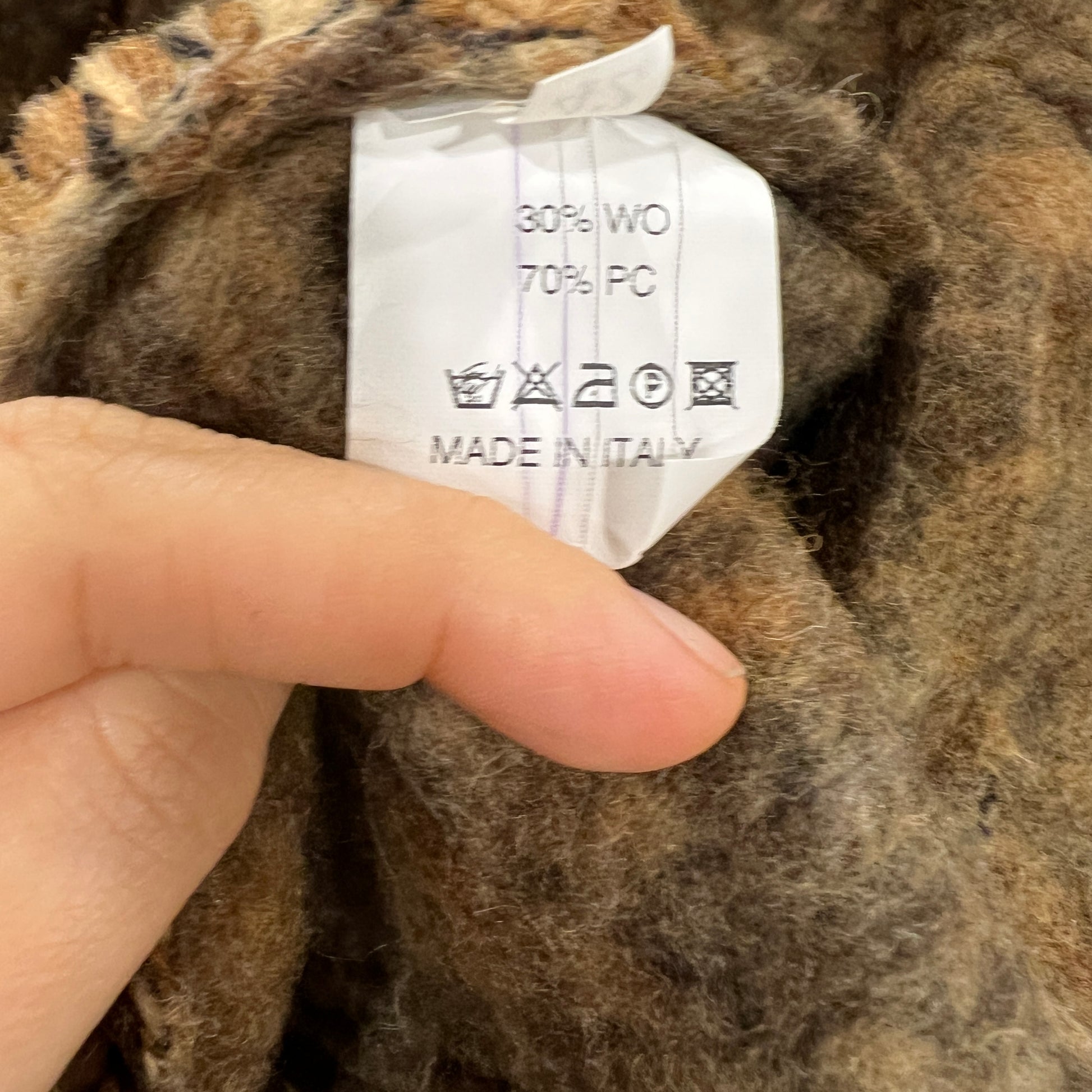 Clothing label on a brown fabric with a hand pointing to it