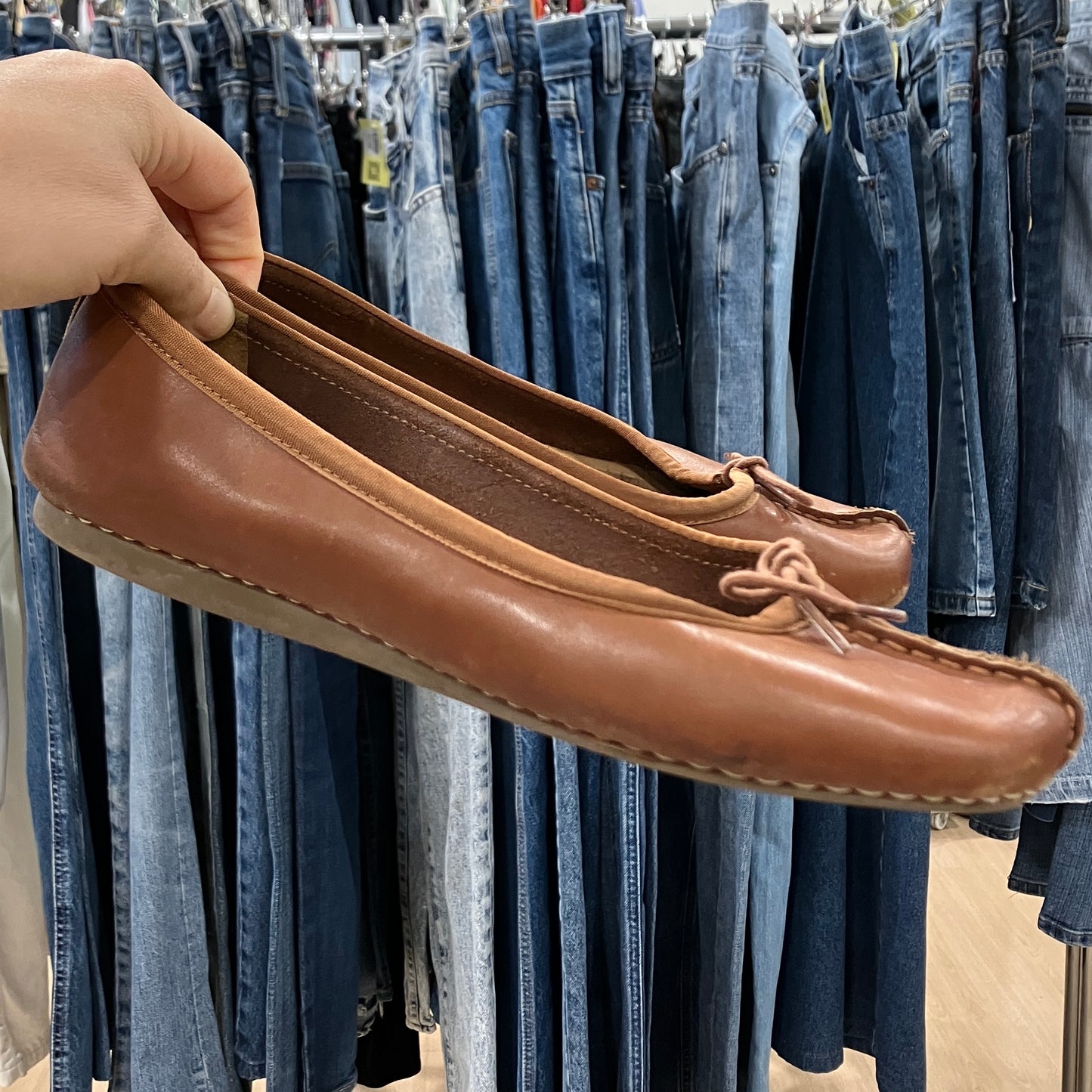 Brown leather shoes held in front of a rack of jeans