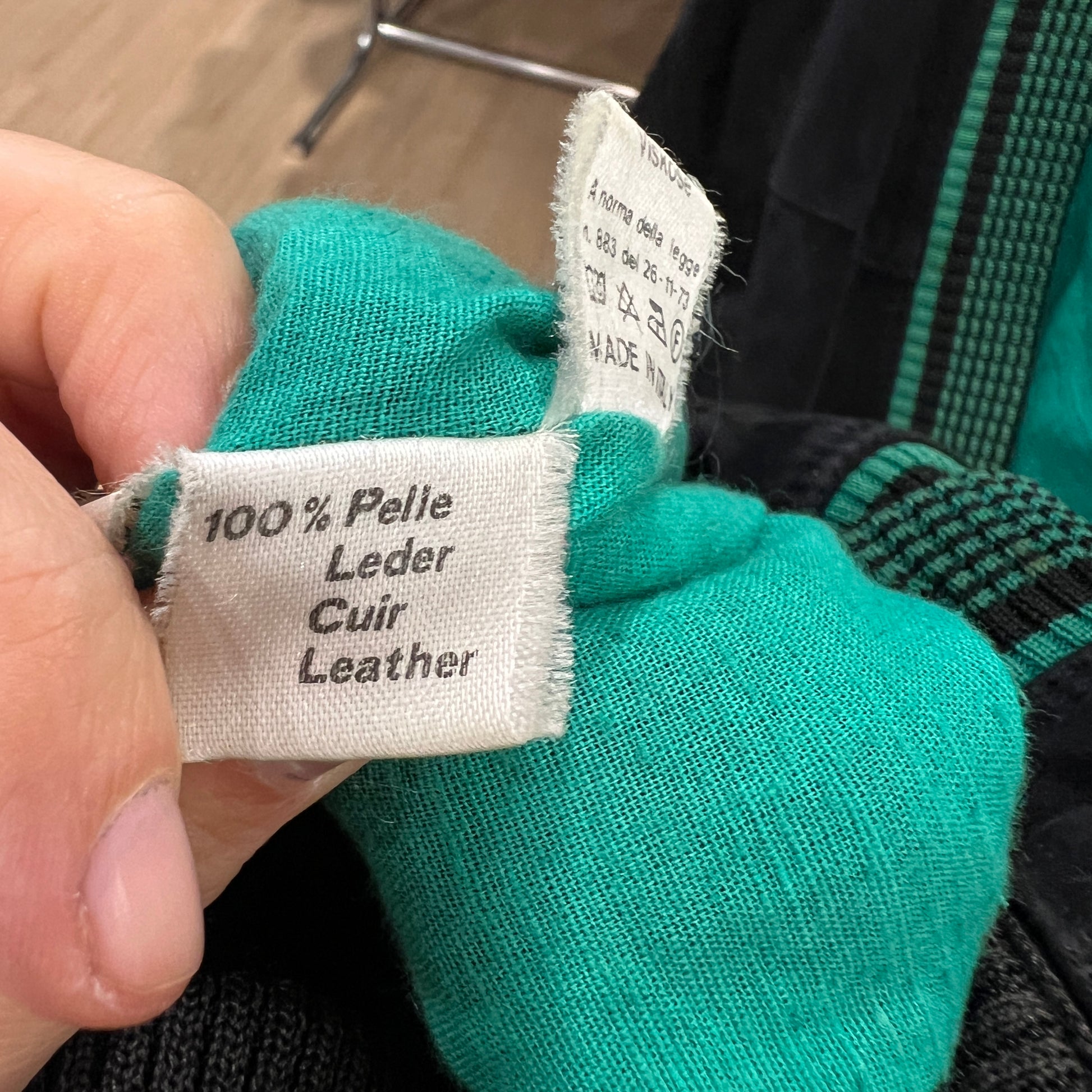 Close-up of a green leather product with a label indicating '100% Pelle Leder Cuir Leather'