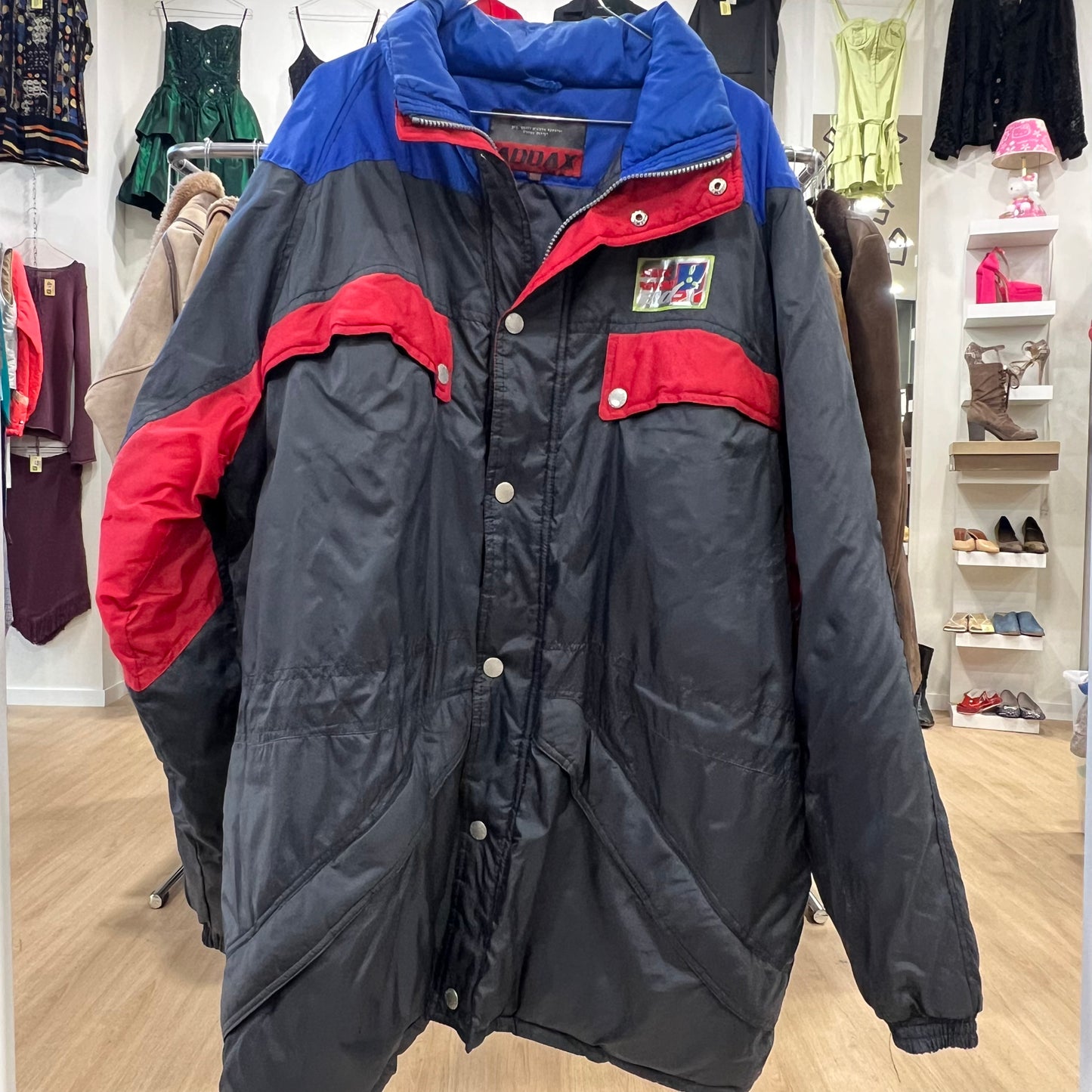 Multicolored jacket with blue, red, and gray sections in a store setting