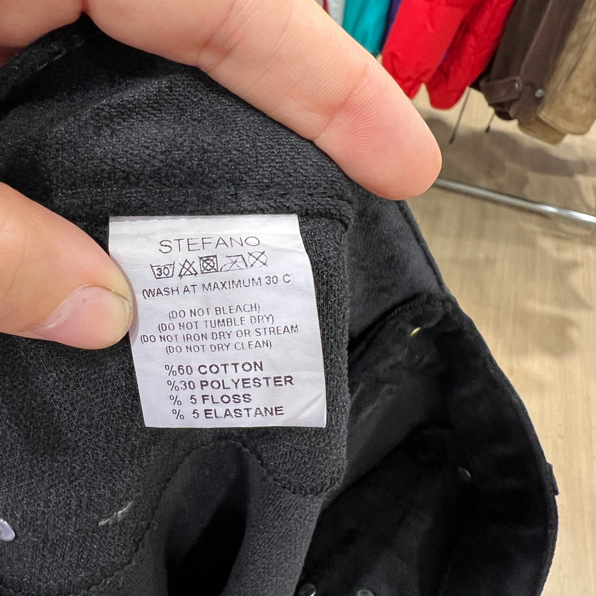 Clothing label on a black garment with text and fabric composition details