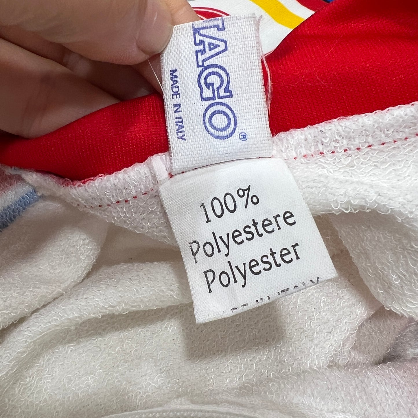 Close-up of a label on a red and white garment with 'Iago' branding