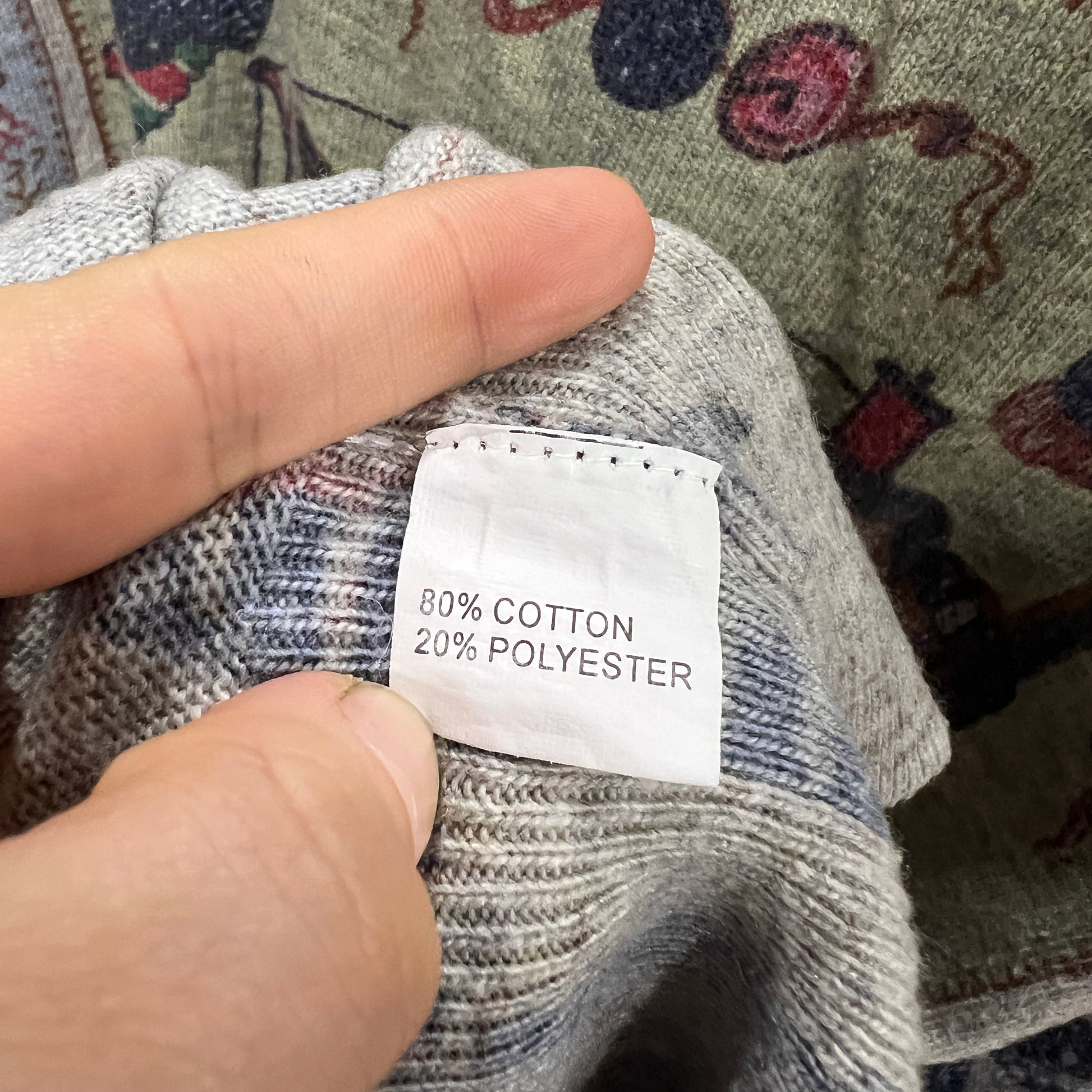 Hand holding a fabric with a '80% Cotton 20% Polyester' label against a patterned background