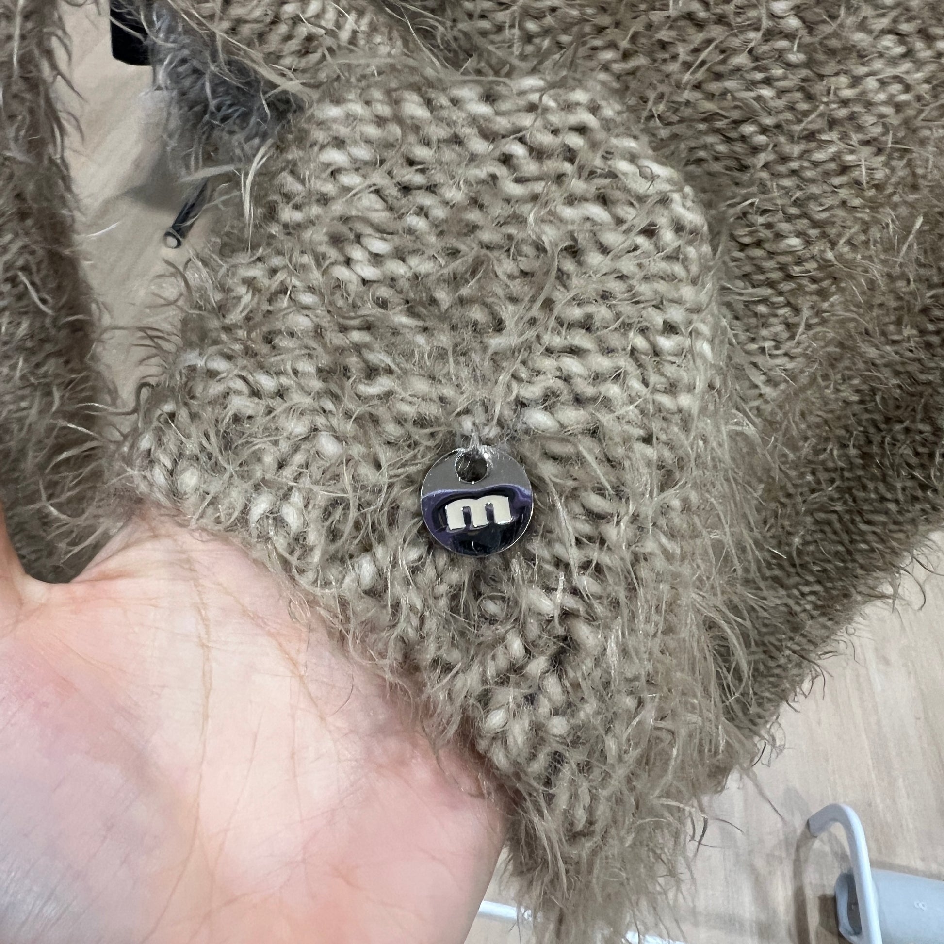 Textured beige fabric with a small M  charm held by a hand