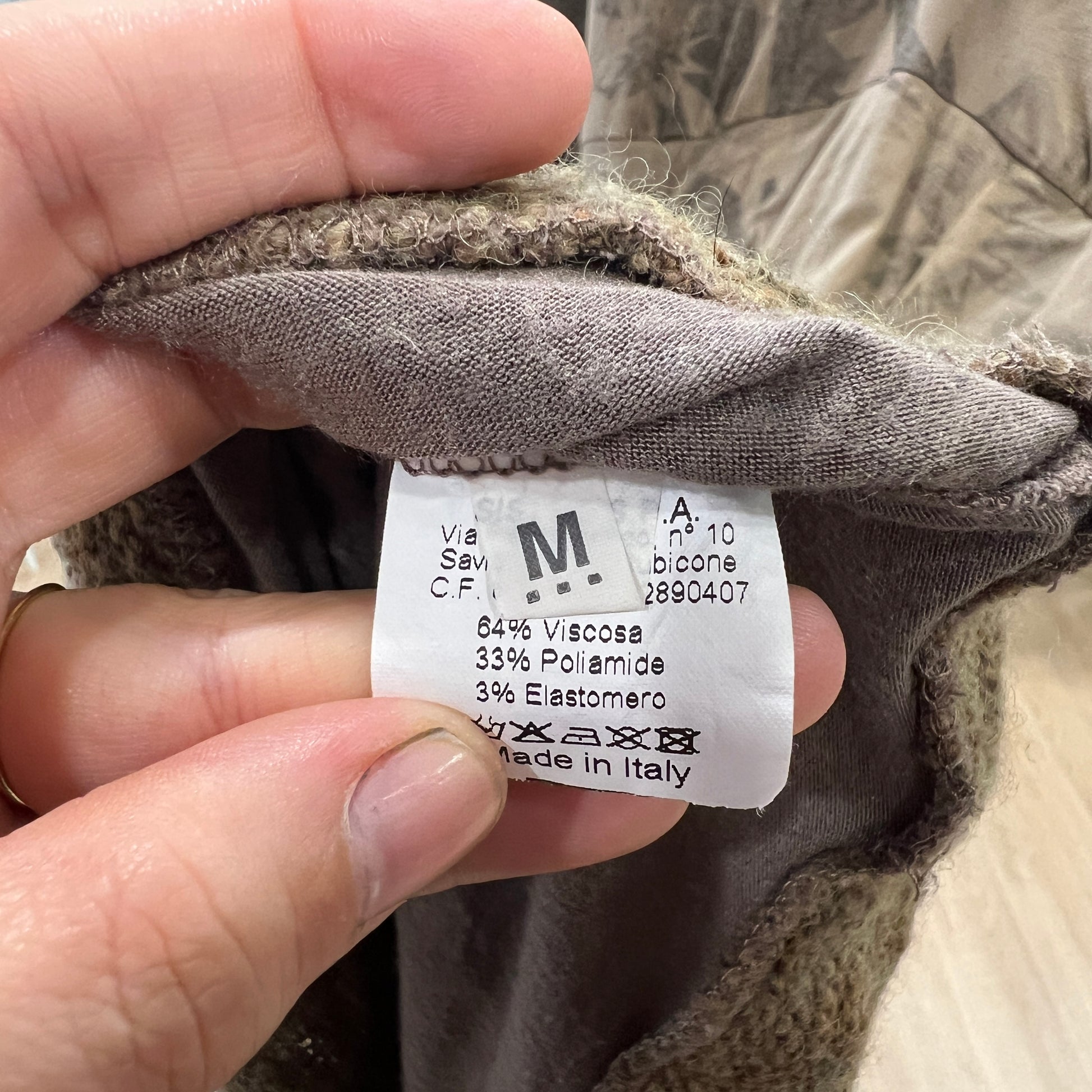 Close-up of a clothing label on a brown fabric with a hand holding it