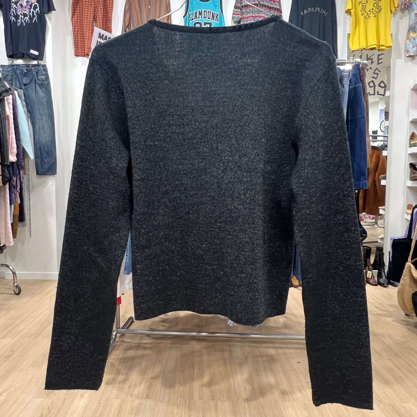 Dark gray sweater in a store setting with clothing racks in the background