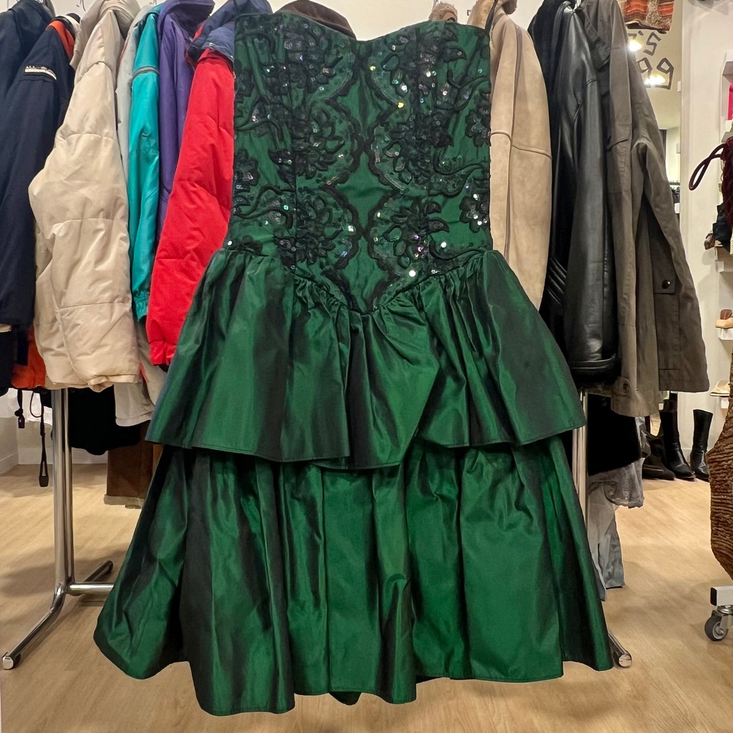 Green dress with sequin detailing on a rack of coats in a store