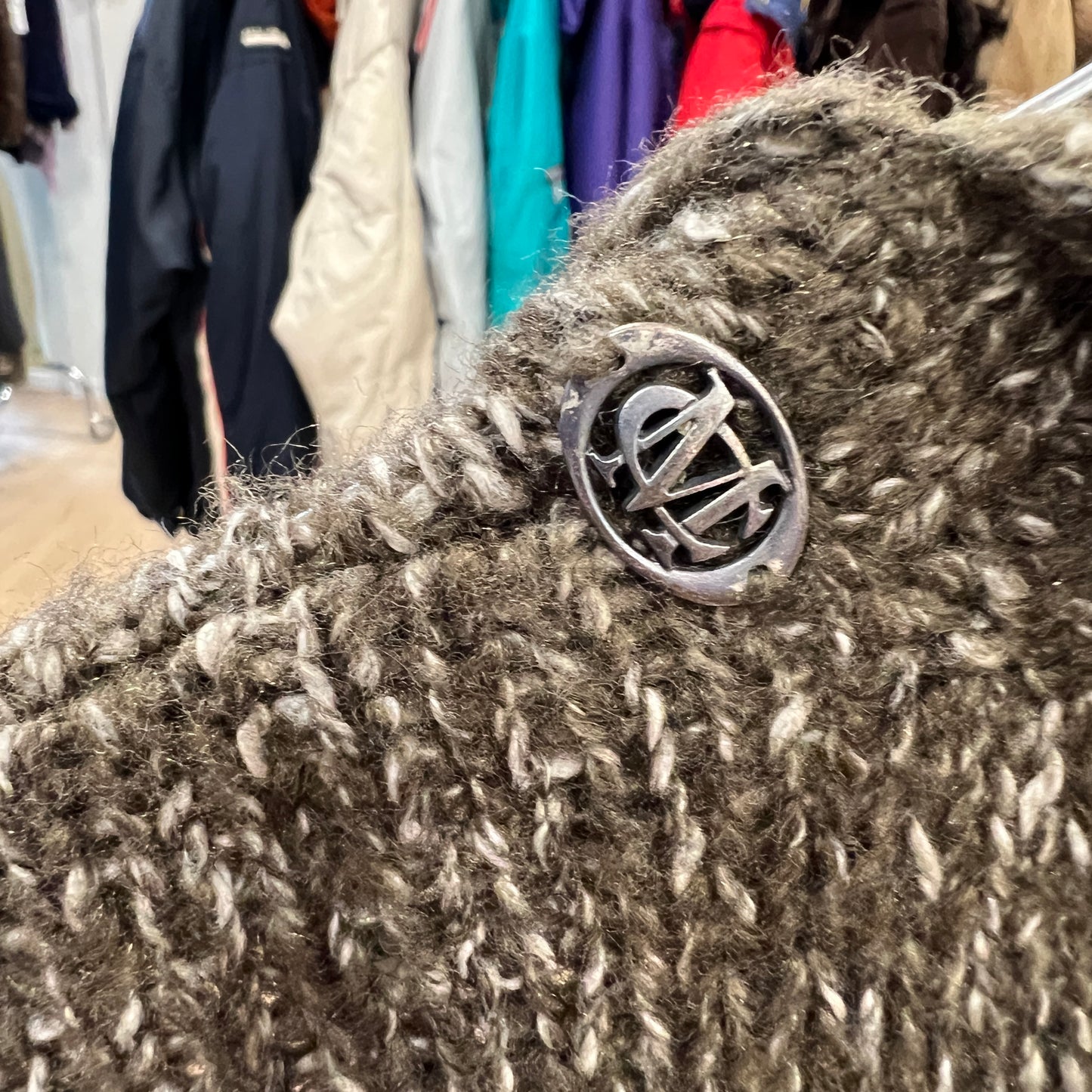 Close-up of a textured fabric with a metal button featuring a logo, set against a background of clothing