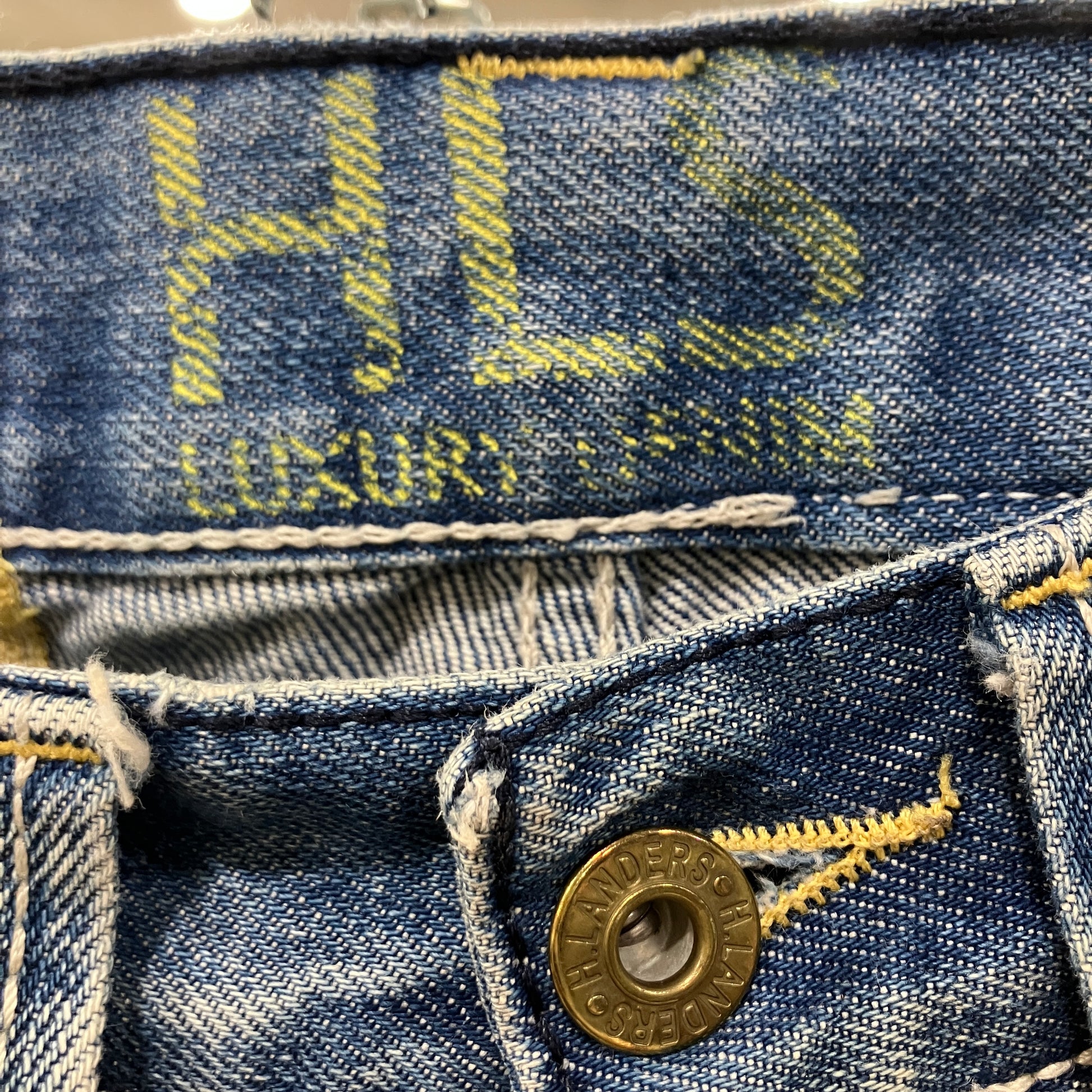 Close-up of a blue denim fabric with a button and 'HLS' branding