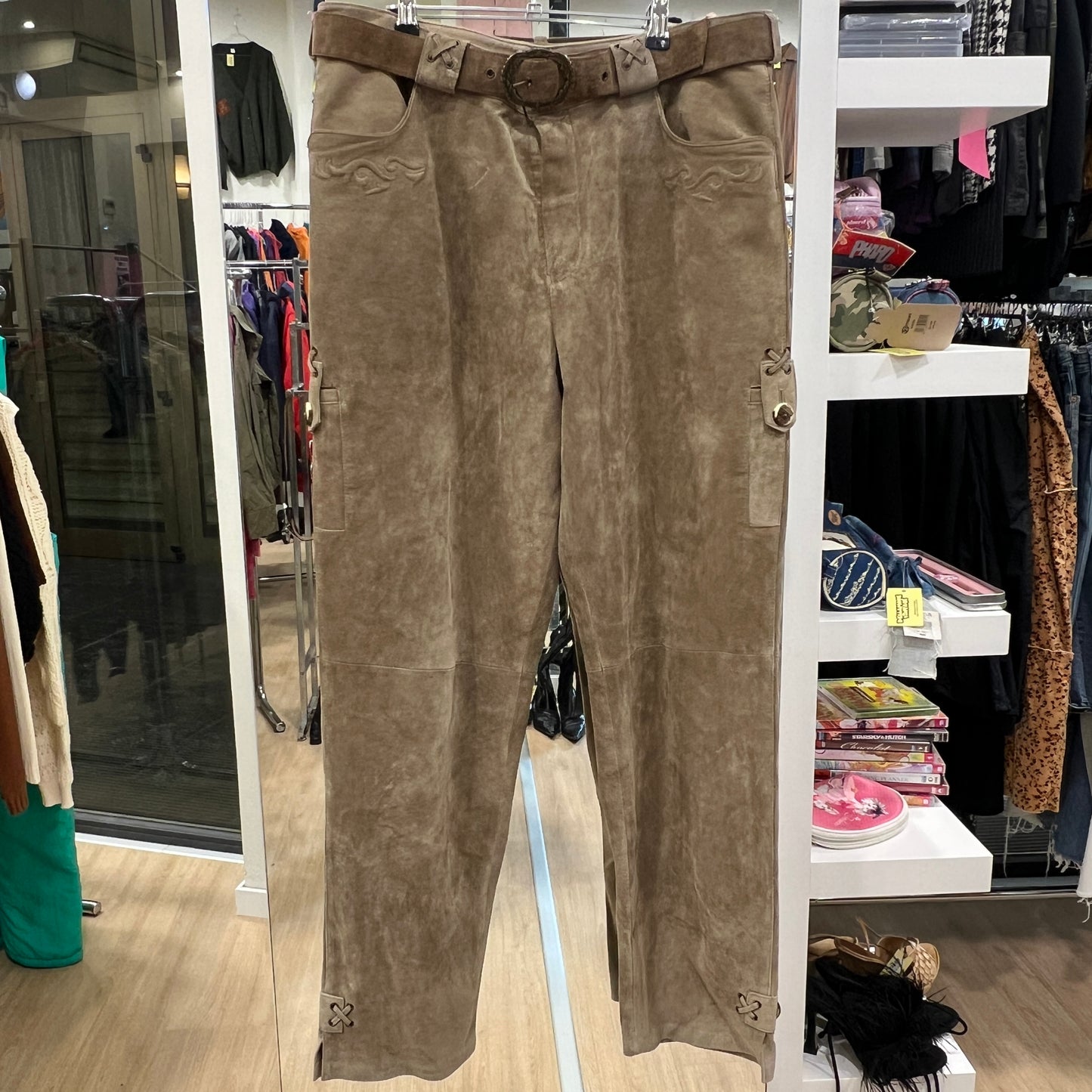 Brown leather pants on a hanger in a store setting with clothing racks and shelves in the background