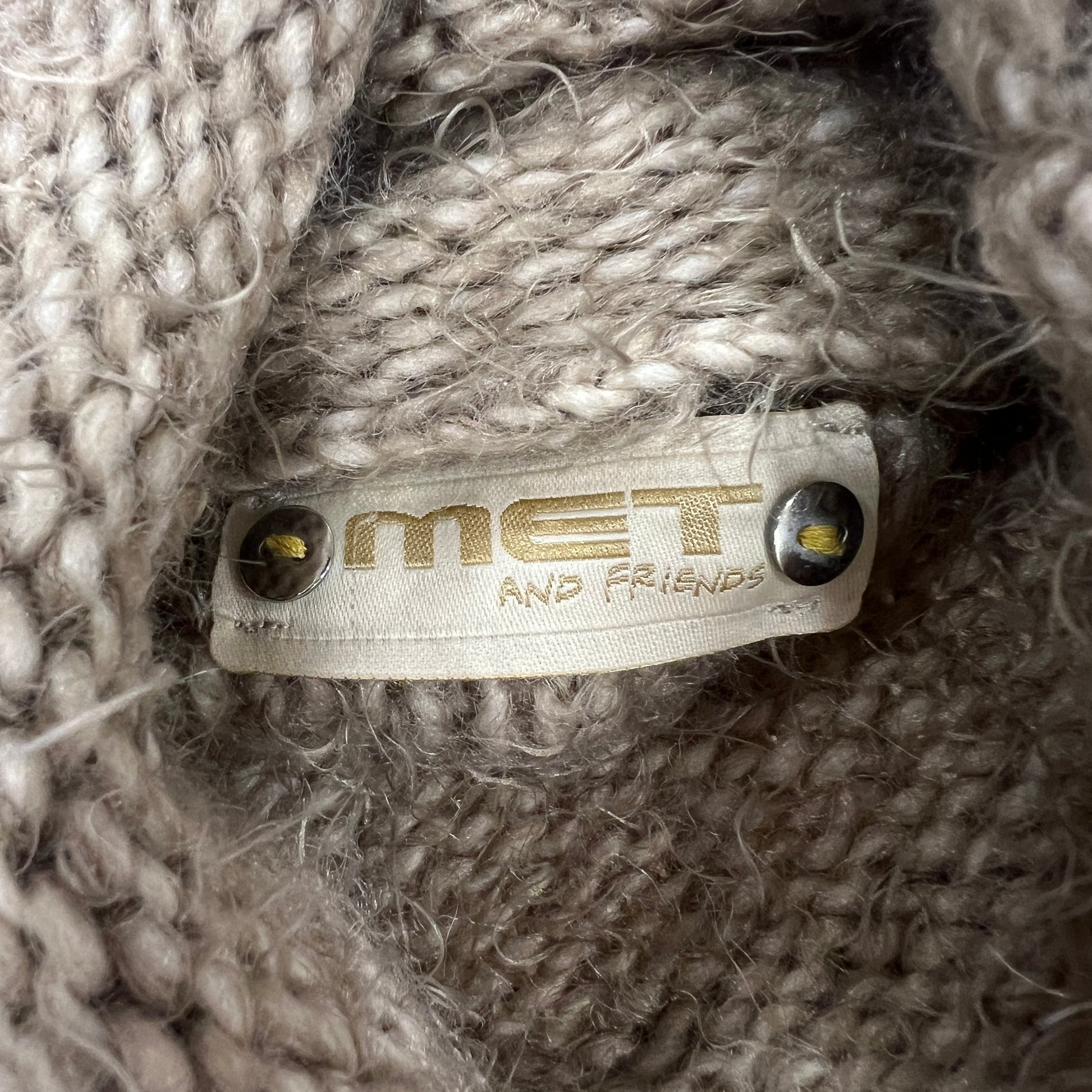 Close-up of a label on a textured fabric surface with 'MET AND FRIENDS' 
