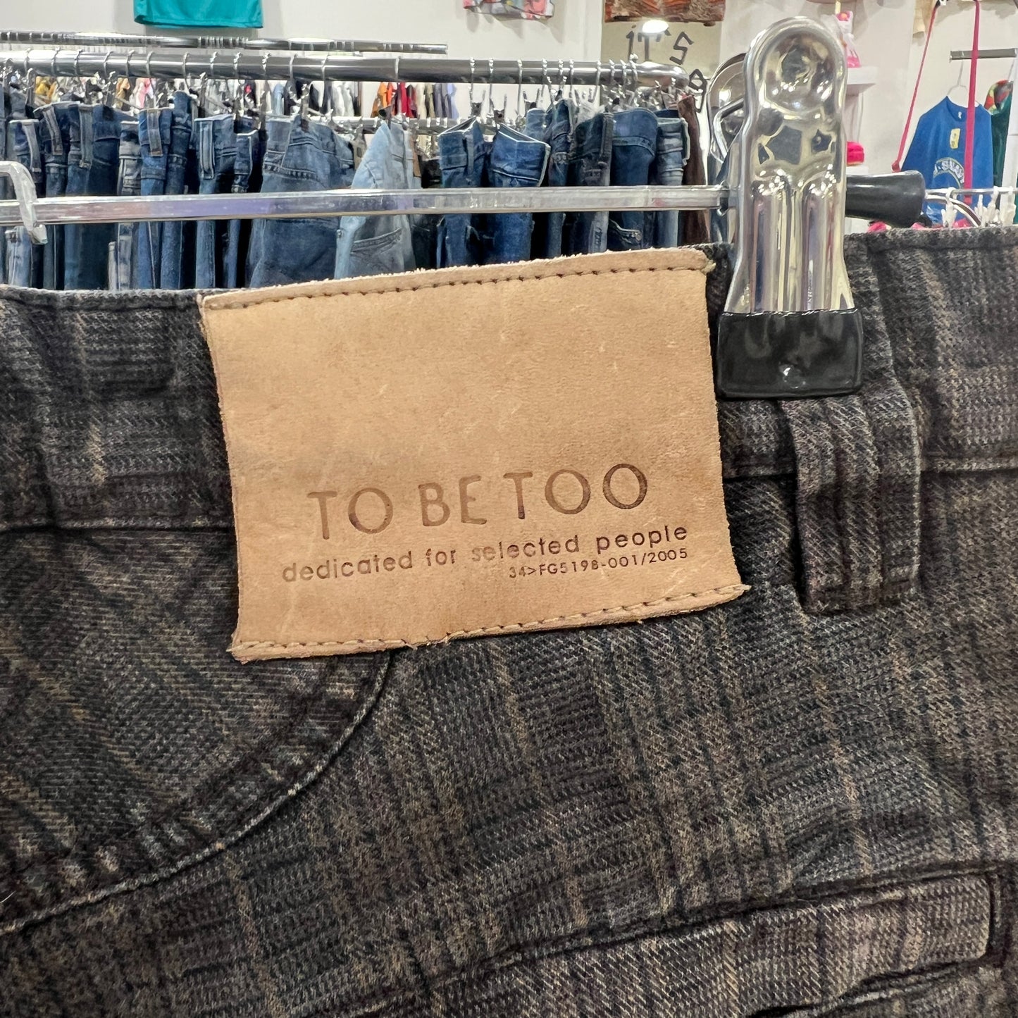 Close-up of a gray denim jacket with a 'TO BE TOO' label in a store setting