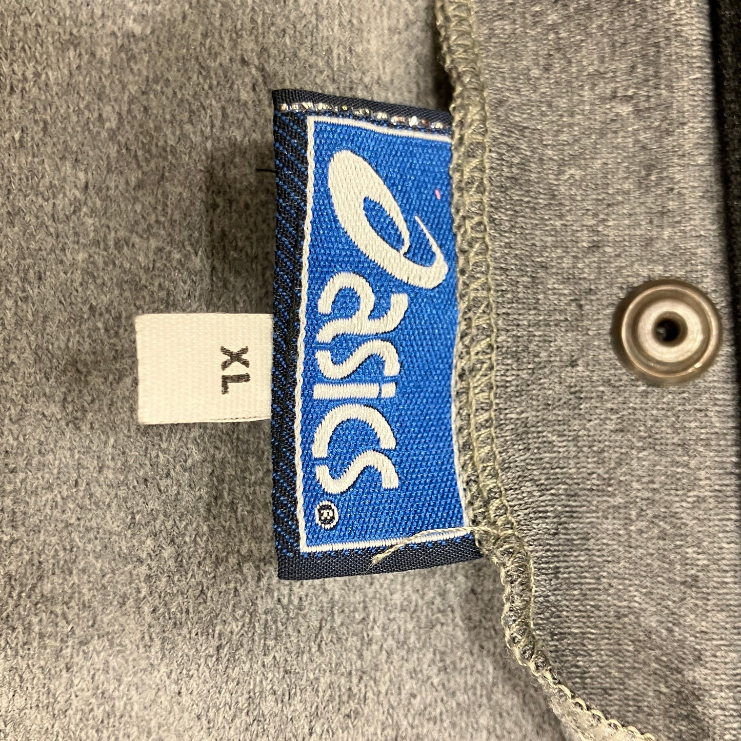 Close-up of a blue Asics label on a gray fabric background