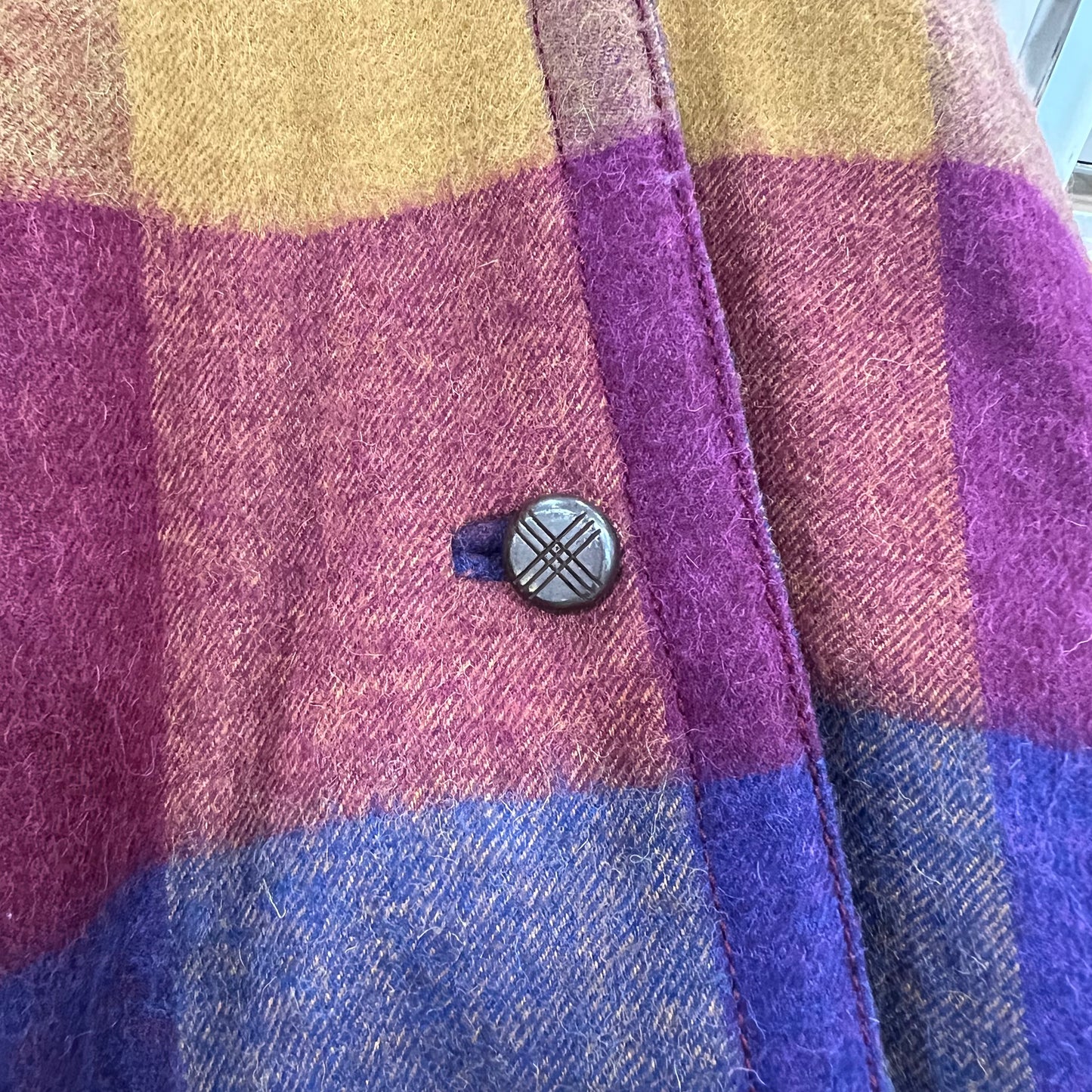 Close-up of a checkered fabric with a button in the center, featuring purple, blue, and yellow colors