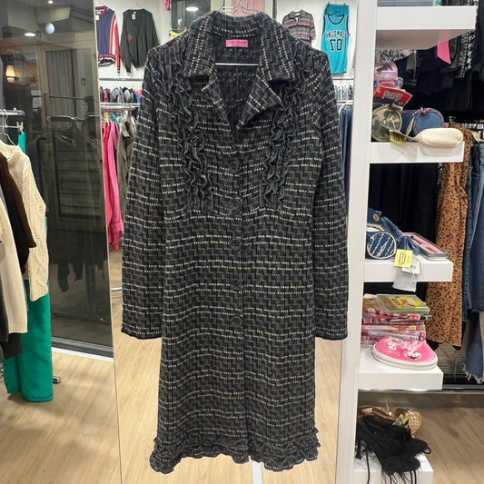 Full-length shot of a black and white textured long coat with ruffled details on the collar and hem, displayed on a hanger inside a vintage clothing store
