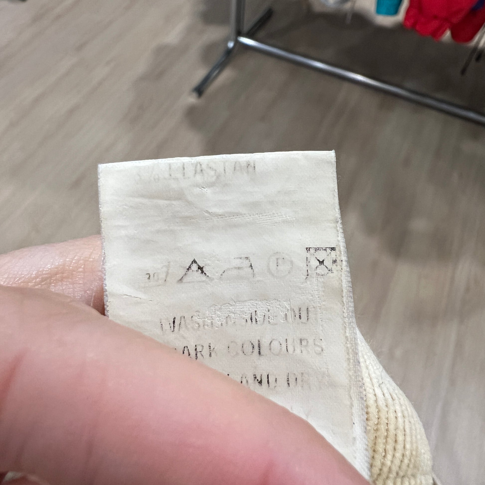 Close-up of a worn white care label on beige corduroy pants, showing faded washing symbols and partially legible text held between two fingers
