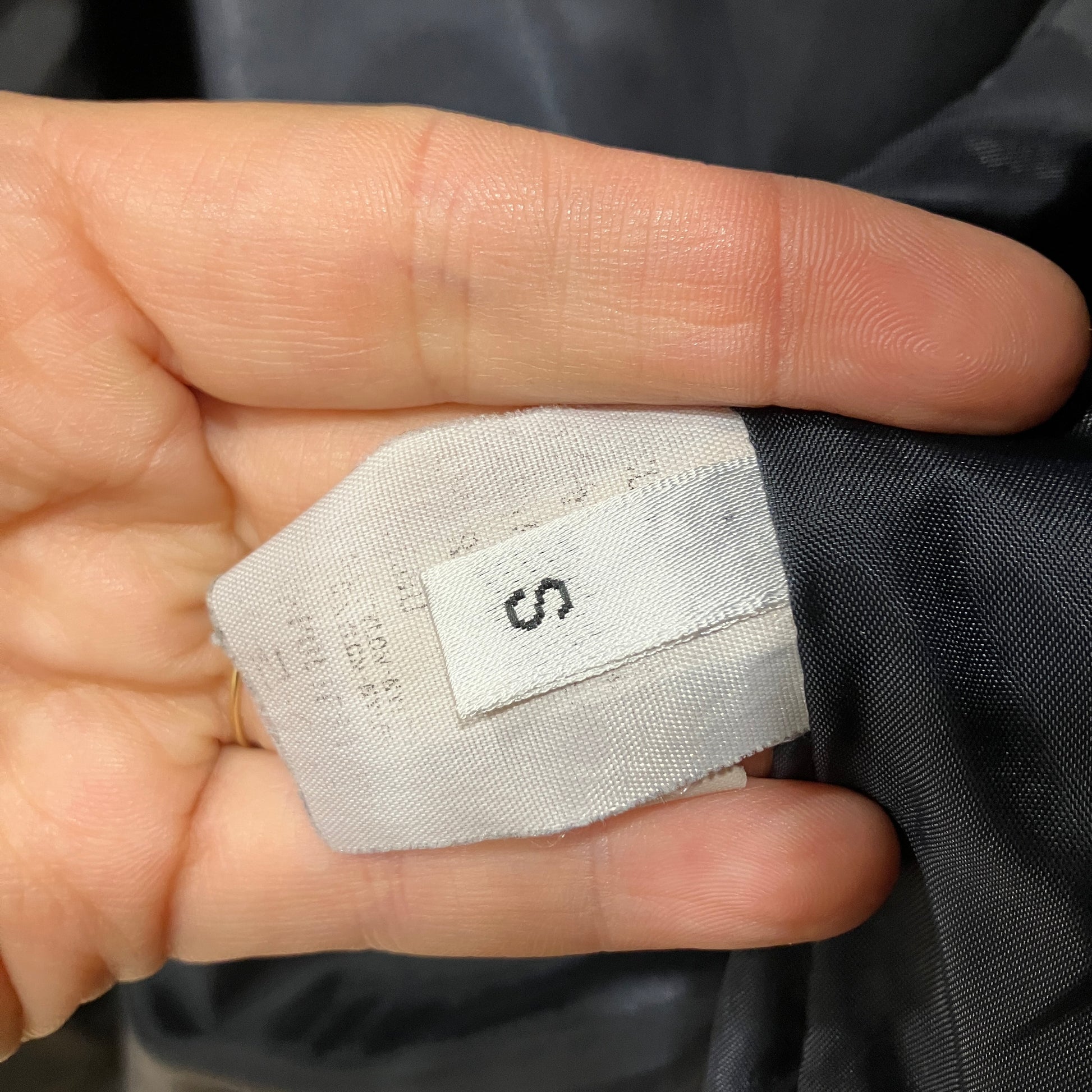 Fabric tag with size 'S' held between fingers against a dark fabric background