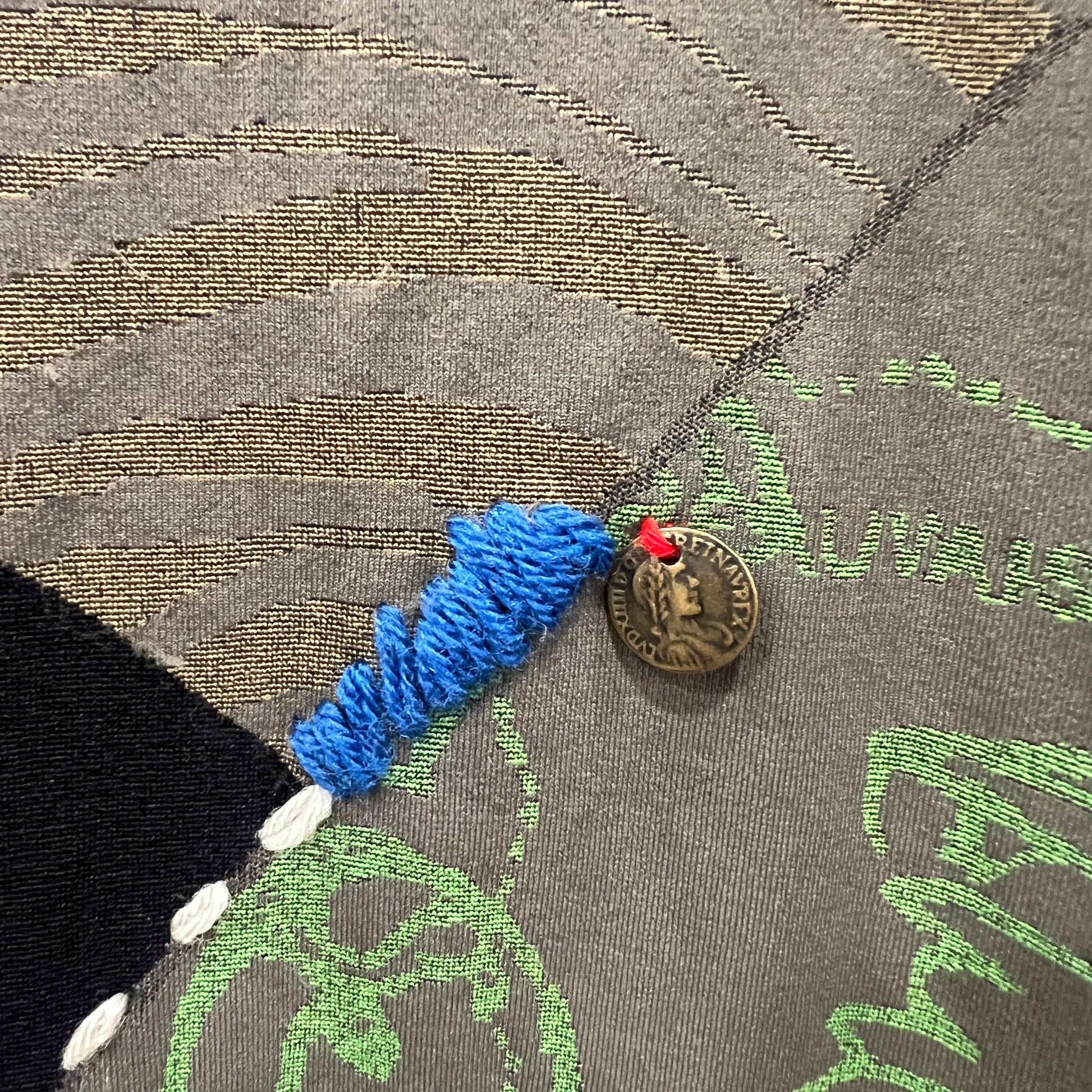 Blue thread with a coin attached to a textured fabric surface