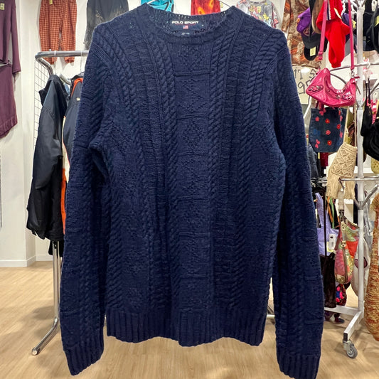 Navy blue cable knit sweater on a rack in a store setting with various items in the background