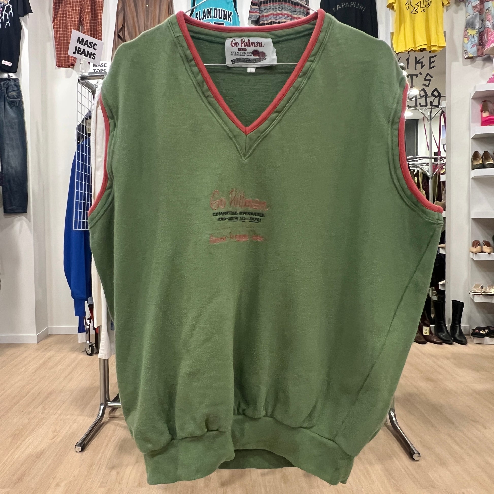 Green sleeveless sweater with red trim on a hanger in a store setting