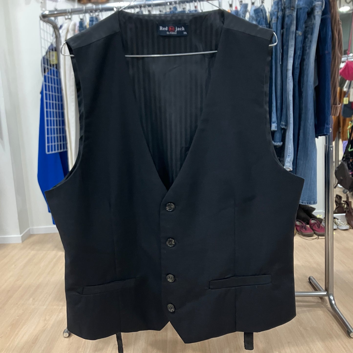 Black vest on a hanger with a clothing rack in the background