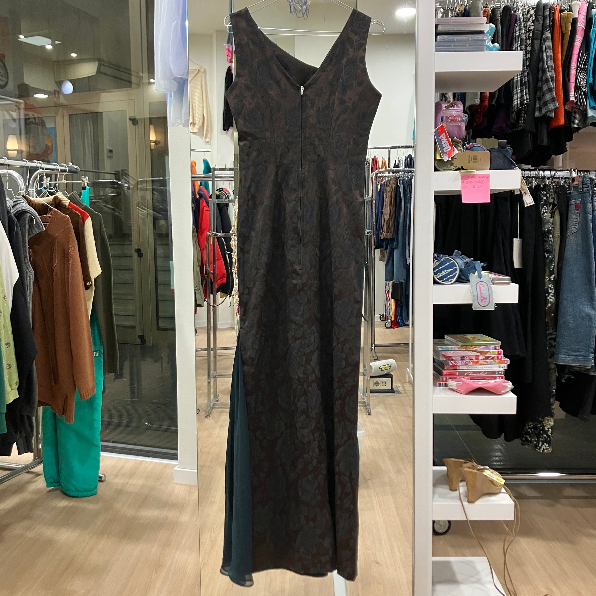 Black patterned dress hanging in a clothing store with racks and shelves in the background