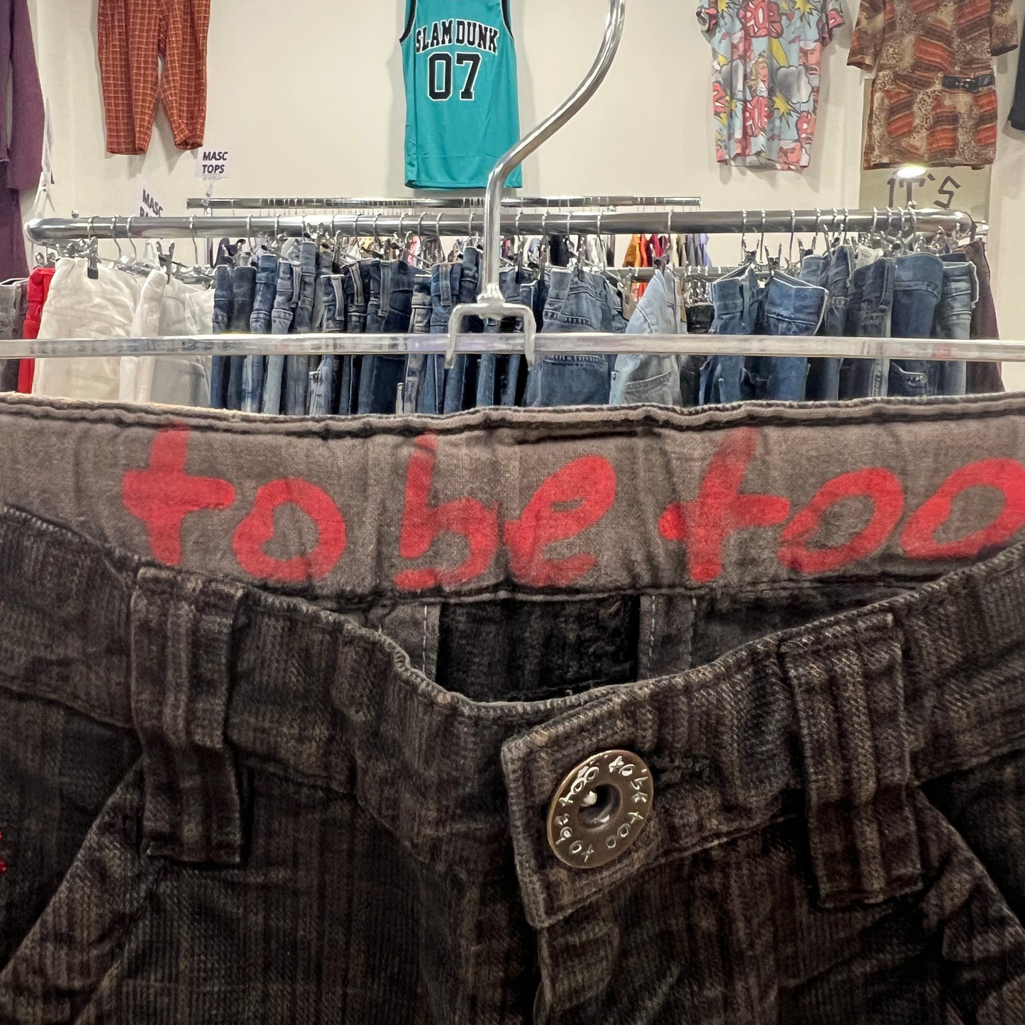 Close-up of a pair of gray pants with red text on a hanger, with a clothing store background