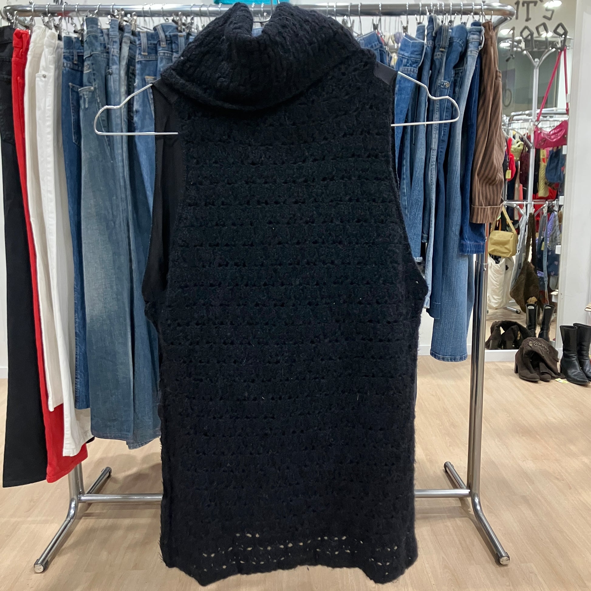 Black knitted vest on a hanger in a clothing store with racks of clothes in the background