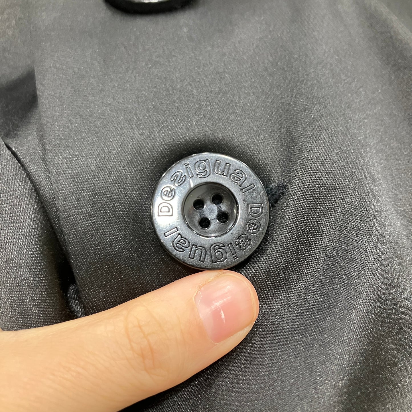Close-up of a button on a gray garment with 'Desigual' branding, touched by a finger