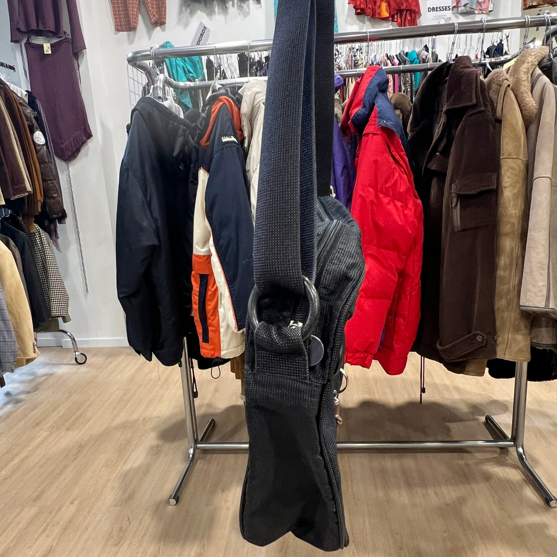Clothing rack with various jackets and a black bag in a store setting