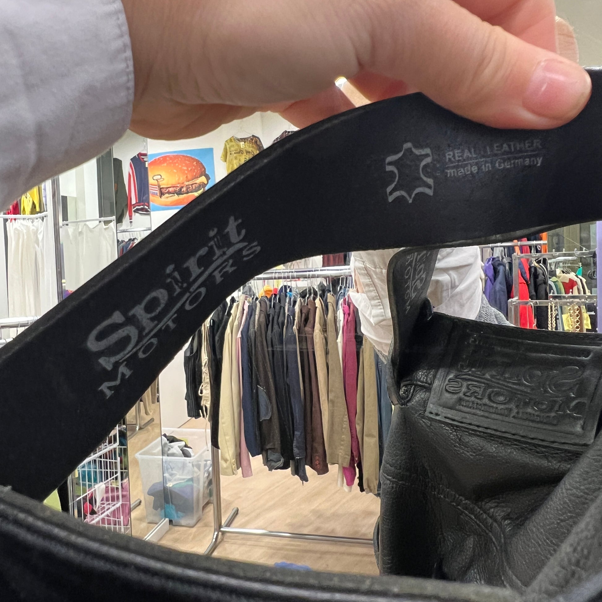 Black leather belt with 'Spirit Motors' branding held up in a clothing store
