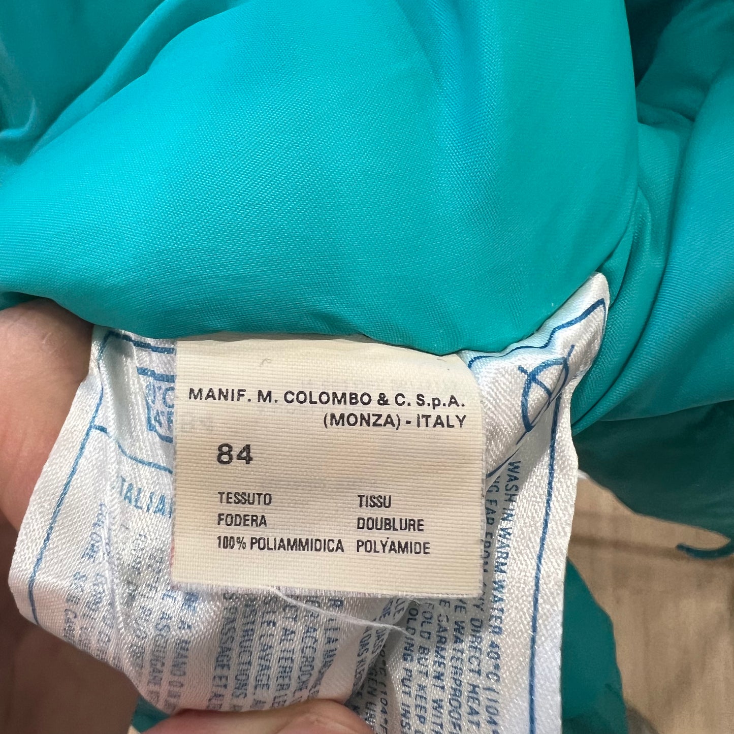 Clothing label on a teal fabric with text and numbers