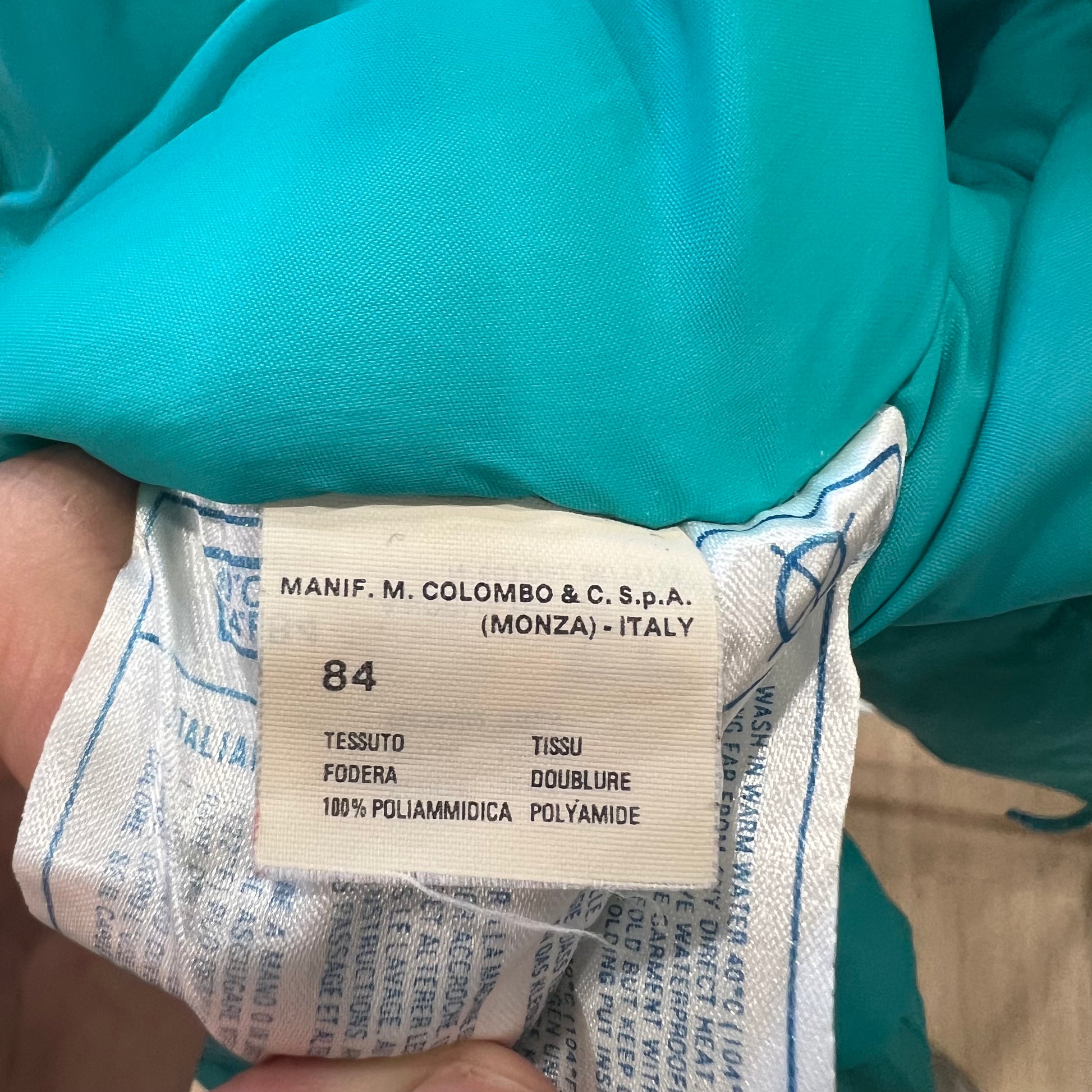 Clothing label on a teal fabric with text and numbers