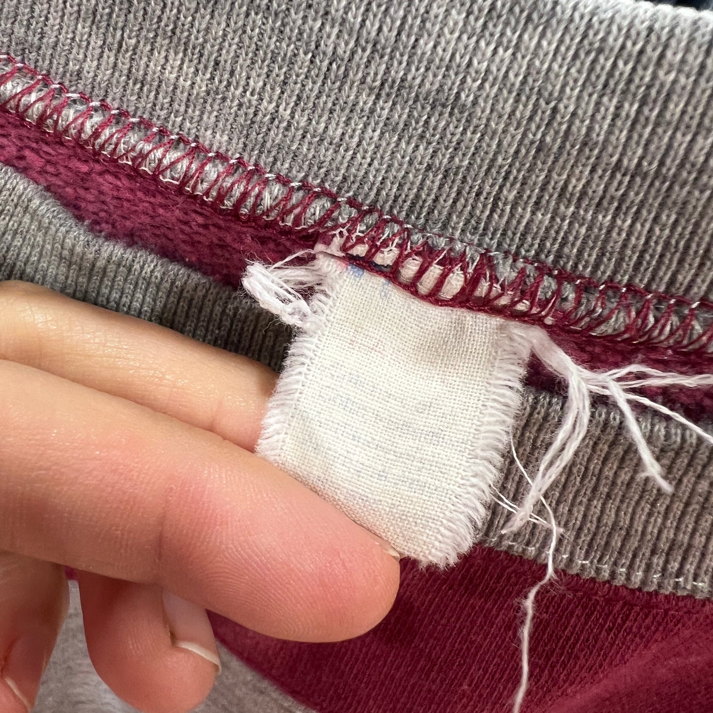 Close-up of a hand holding a piece of frayed fabric with a striped garment background