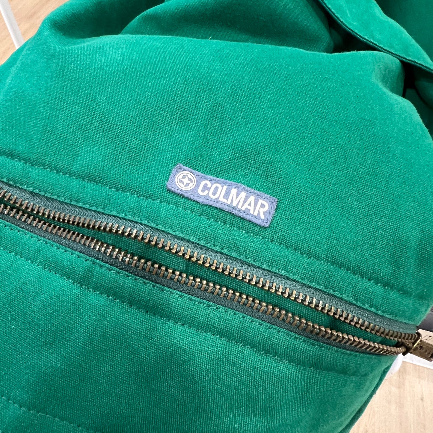 Green jacket with a Colmar label on a wooden surface