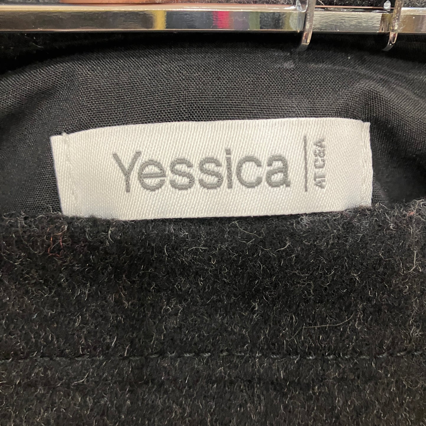 Close-up of a black garment with a 'Yessica' label on a dark background