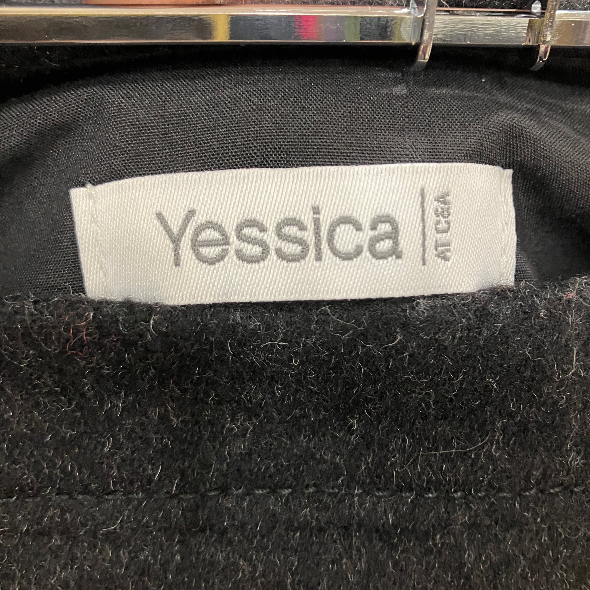 Close-up of a black garment with a 'Yessica' label on a dark background