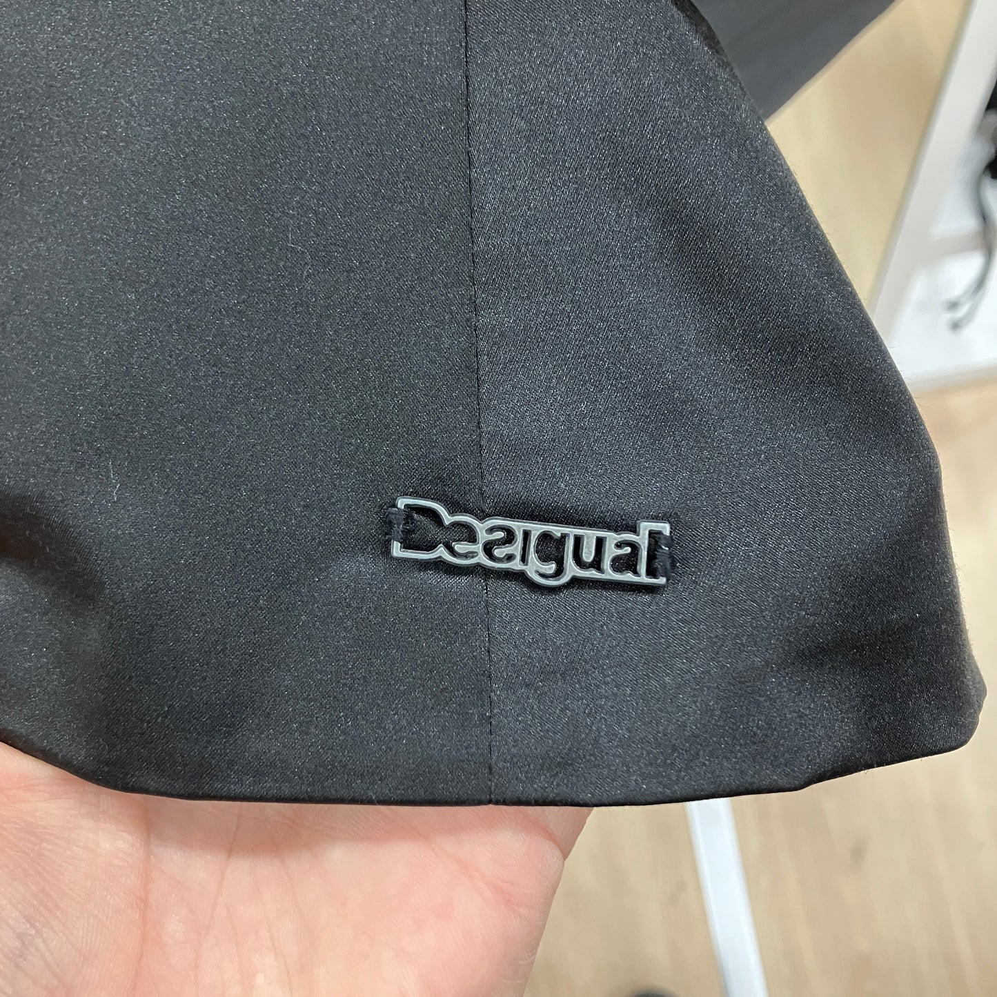 Black cap with 'Desigual' logo held by a hand on a blurred background
