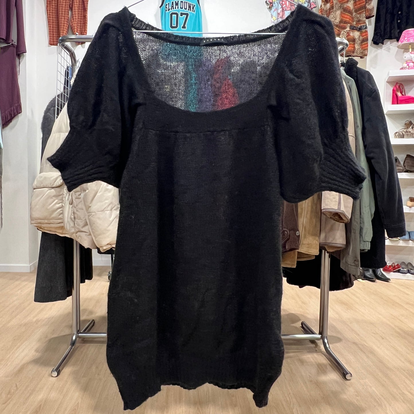 Black sweater on a rack in a store setting with various clothing items in the background