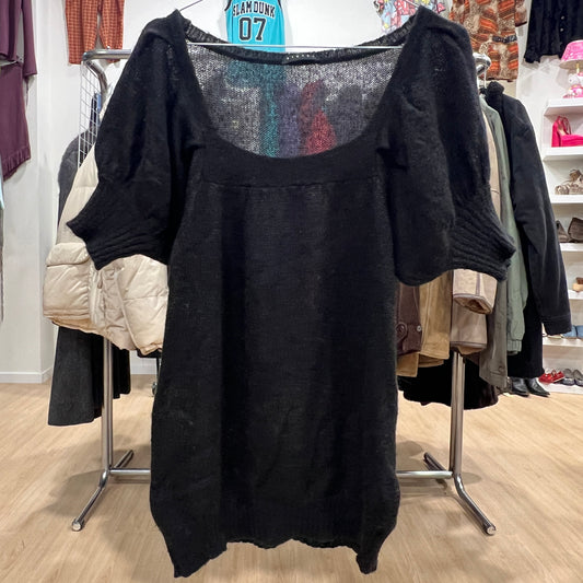 Black sweater on a rack in a store setting with various clothing items in the background