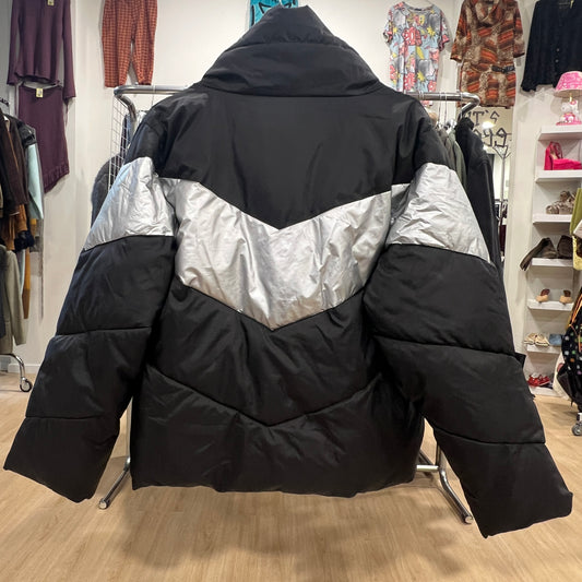 Black and silver puffer jacket on a hanger in a store setting with clothing racks and shelves in the background