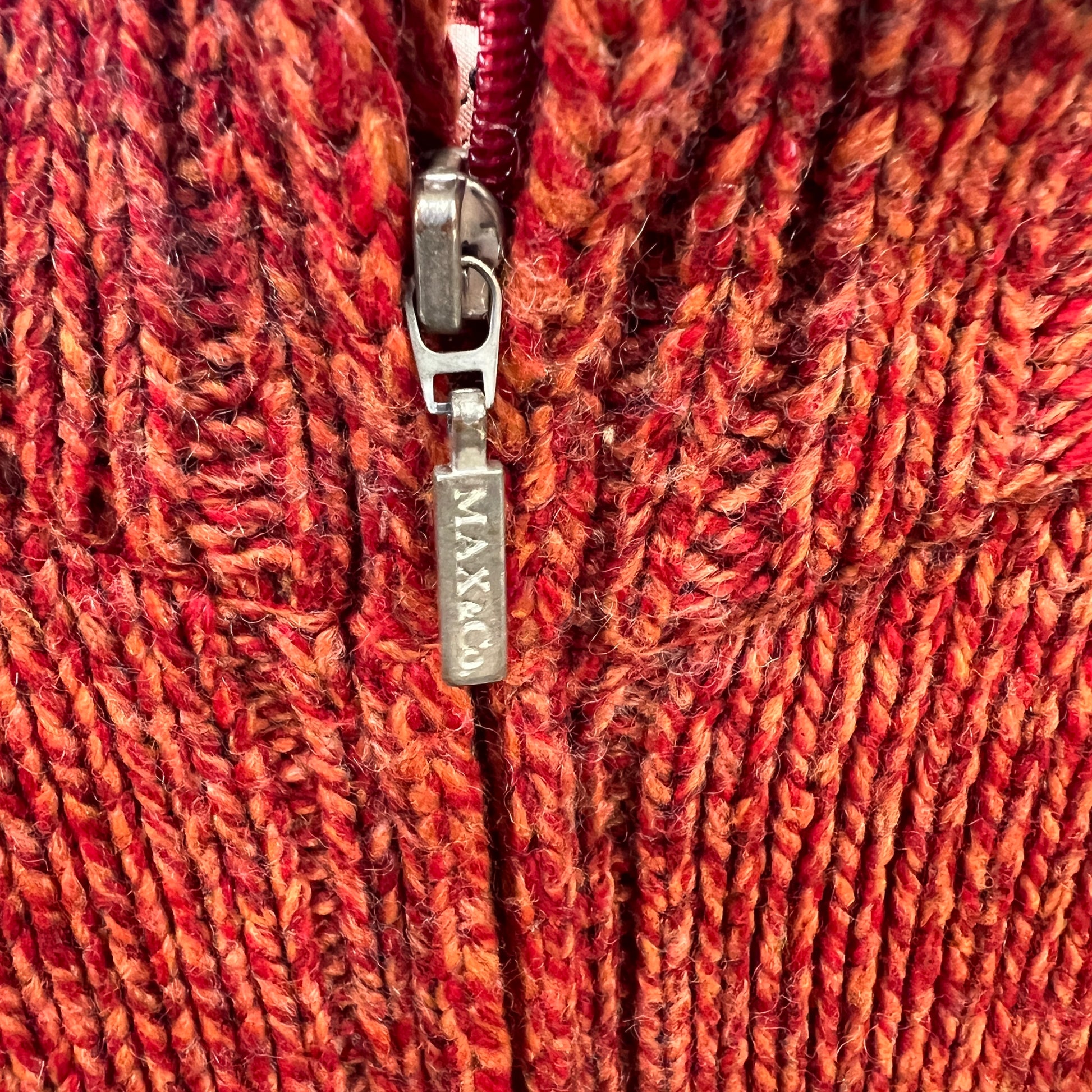 Close-up of a red textured fabric with a zipper, featuring the brand 'MAX&Co'