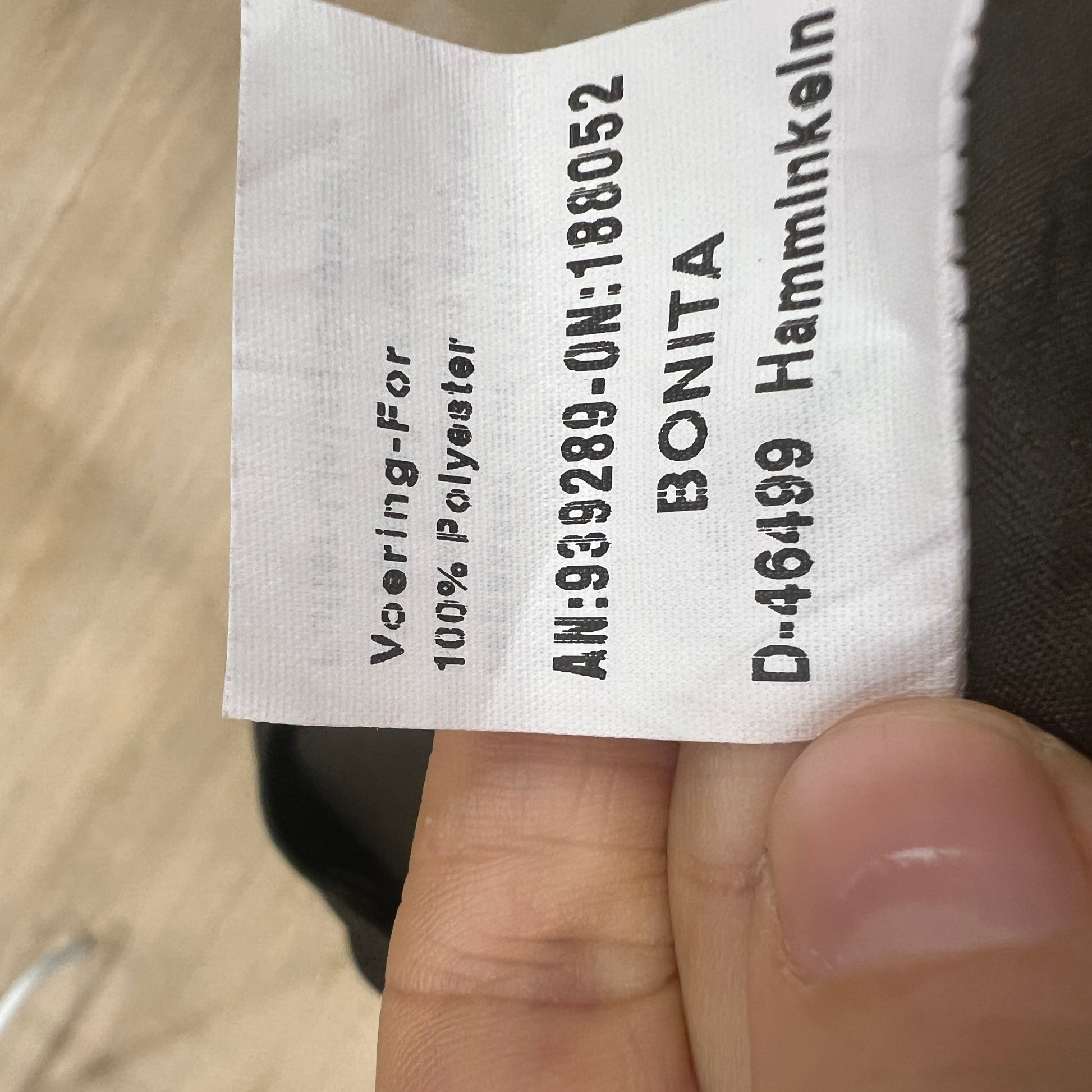 Clothing label held by a hand with text on a wooden surface