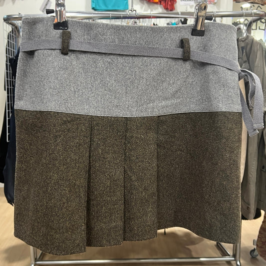 Front view of a two-tone wool skirt with a grey waistband and tie belt and a brown pleated lower panel, displayed on a hanger inside a vintage clothing store
