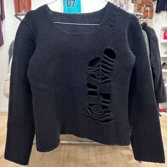 Black sweater with a decorative cutout design on a hanger in a store setting