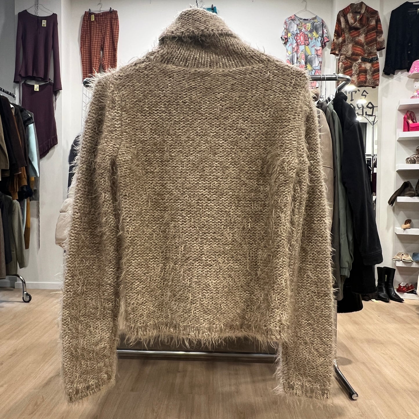 Beige fuzzy cardigan on a hanger in a clothing store setting