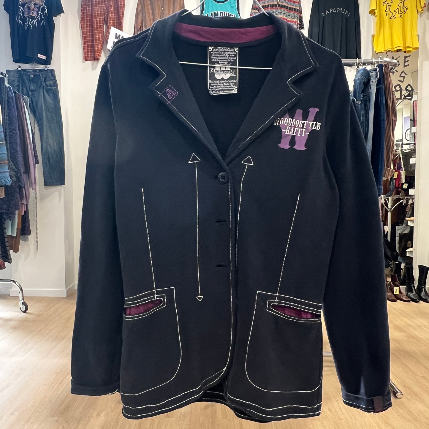 Black jacket with white stitching and purple accents on a clothing rack