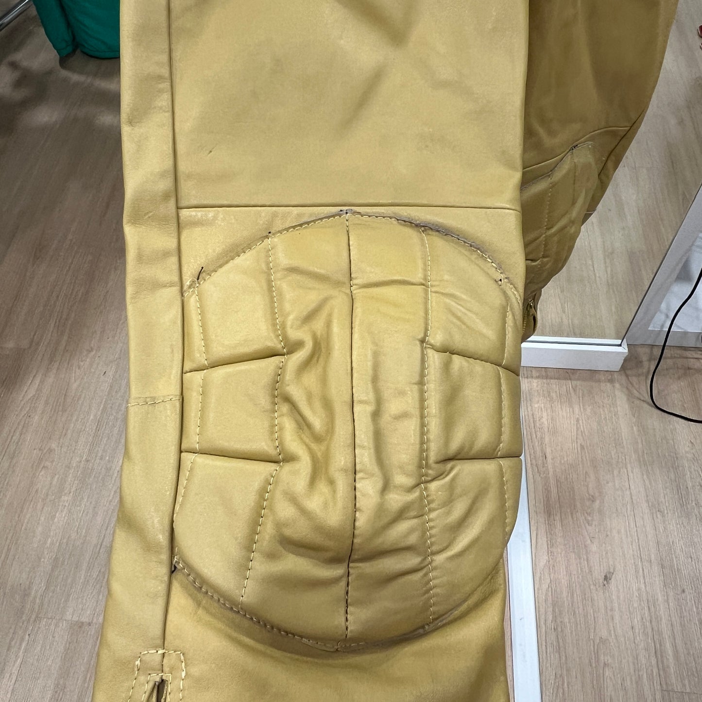 Close-up of the padded knee panel on a yellow work-style jumpsuit, showing stitched protective sections and textured reinforcement on the front of the leg
