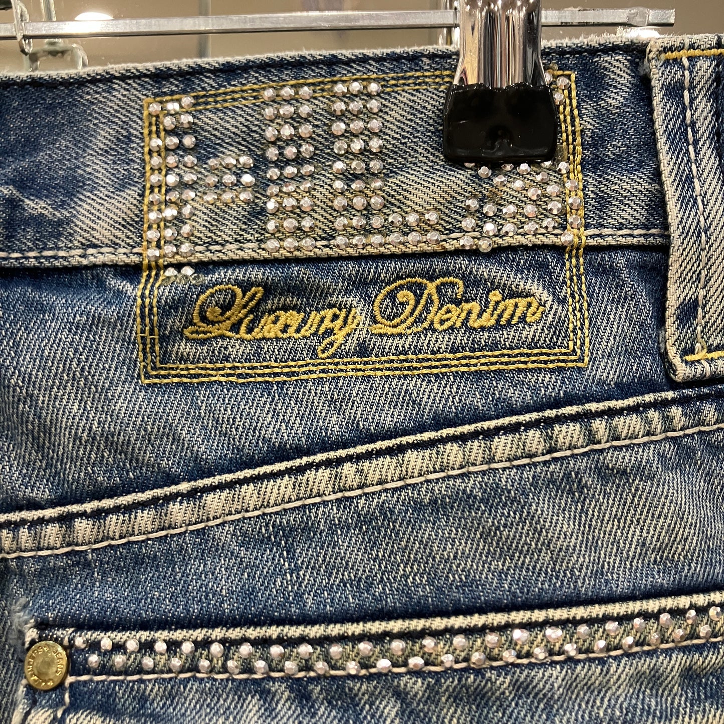 Close-up of a blue denim product with 'Luxury Denim' branding and rhinestone embellishments