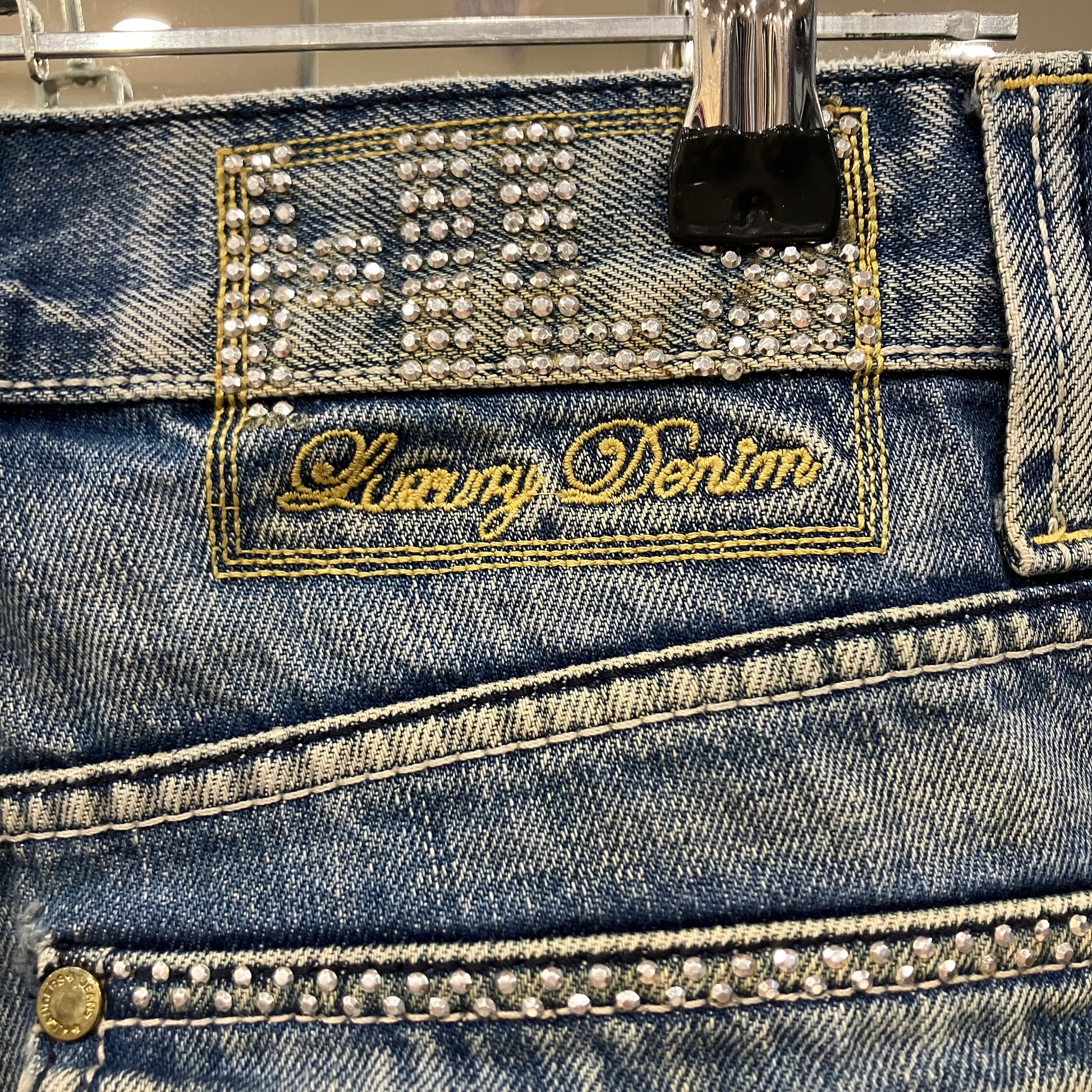 Close-up of a blue denim product with 'Luxury Denim' branding and rhinestone embellishments